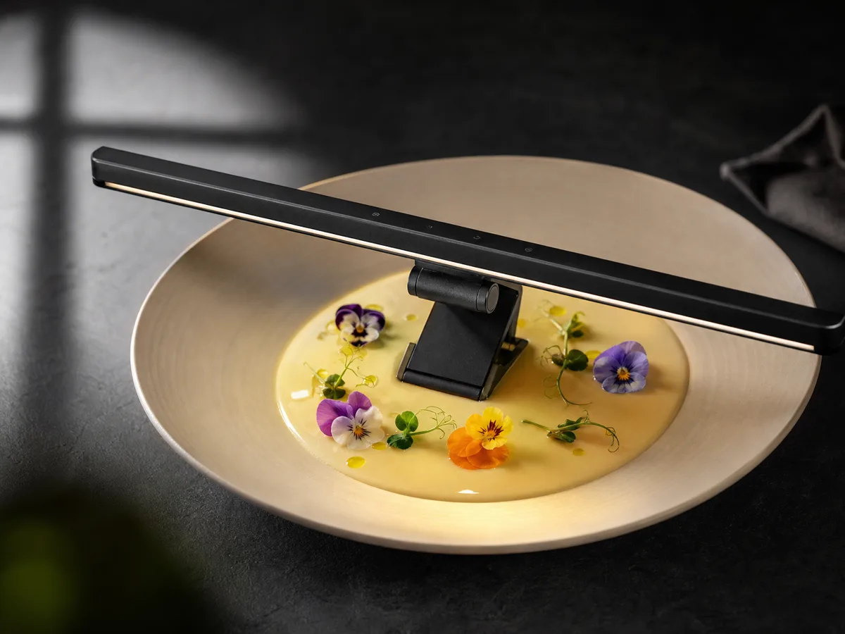 Quntis light bar standing in a shallow pool of velouté on a wide plate, garnished with edible flowers